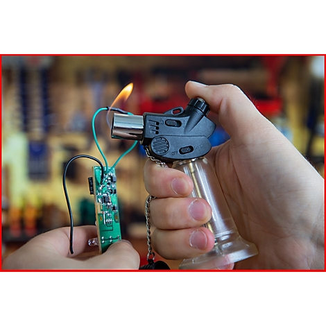 Person hält eine Lötlampe mit Feuer. Eine Platine ist mit Drähten angeschlossen.